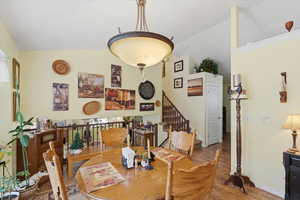 Dining area with wood finished floors, stairs, and high vaulted ceiling