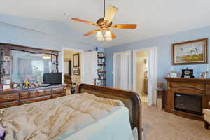 Bedroom featuring light colored carpet, lofted ceiling, ceiling fan, and a glass covered fireplace