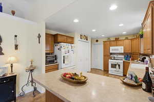 Kitchen featuring light countertops, white appliances, brown cabinets, recessed lighting, and a peninsula
