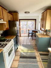 Kitchen featuring butcher block countertops, gas range gas stove, light tile patterned floors, under cabinet range hood, and brown cabinets