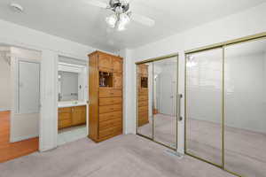 Unfurnished bedroom featuring multiple closets, light carpet, ceiling fan, ensuite bathroom, and a textured ceiling