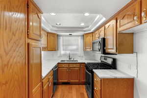 Kitchen with appliances with stainless steel finishes, backsplash, a raised ceiling, light wood-style flooring, and recessed lighting