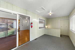 Carpeted spare room with attic access, wood walls, and a textured ceiling