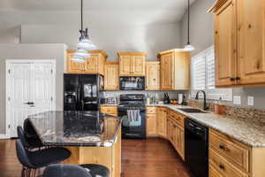 Kitchen with black appliances, dark stone countertops, dark wood finished floors, a kitchen breakfast bar, and pendant lighting