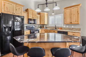 Kitchen featuring black appliances, dark stone counters, light brown cabinetry, and a kitchen island