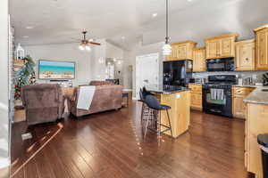 Kitchen with light brown cabinets, black appliances, a breakfast bar, open floor plan, and a center island