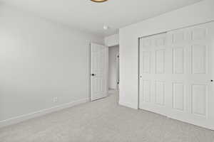 Unfurnished bedroom featuring light carpet and a closet