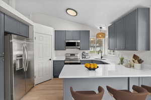 Kitchen with appliances with stainless steel finishes, a breakfast bar, a peninsula, light wood-style floors, and light stone counters