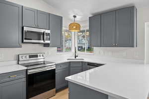 Kitchen featuring stainless steel appliances, gray cabinetry, decorative light fixtures, a peninsula, and light stone countertops