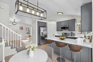 Kitchen featuring hanging light fixtures, stainless steel appliances, a peninsula, gray cabinetry, and a breakfast bar area