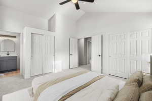 Bedroom featuring multiple closets, ensuite bath, high vaulted ceiling, light colored carpet, and a ceiling fan