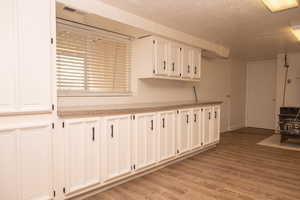 Kitchen with a wood stove, white cabinetry, light wood finished floors, a textured ceiling, and light countertops