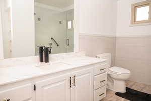 Full bathroom with a stall shower, vanity, light wood-style flooring, tile walls, and wainscoting