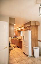 Kitchen featuring white refrigerator with ice dispenser, light tile patterned flooring, tasteful backsplash, brown cabinets, and a textured ceiling