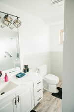 Full bathroom with vanity, light wood-type flooring, tile walls, and a wainscoted wall