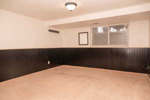 Spare room featuring wood walls, wainscoting, a textured ceiling, and carpet flooring