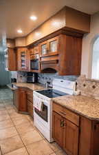 Kitchen with electric range, brown cabinetry, glass insert cabinets, tasteful backsplash, and arched walkways