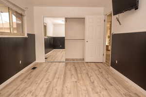 Empty room featuring wainscoting, light wood finished floors, and wood walls