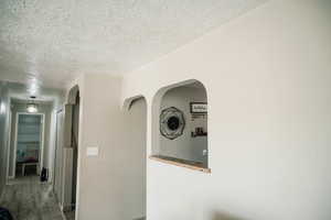 Hall with a textured ceiling, arched walkways, and wood finished floors