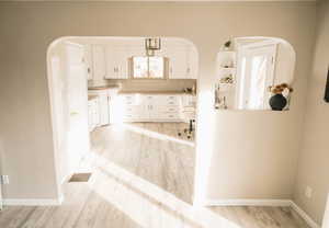 Kitchen with arched walkways, white cabinetry, light wood-style floors, and light countertops