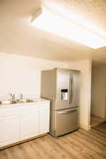 Kitchen featuring stainless steel fridge, a textured ceiling, white cabinets, light countertops, and light wood-style flooring