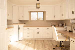 Kitchen with built in study area, pendant lighting, white cabinetry, light countertops, and light wood-type flooring