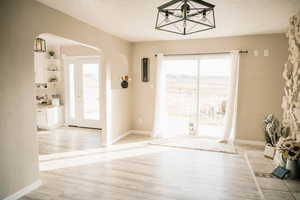 Doorway with arched walkways, wood finished floors, healthy amount of natural light, and a textured ceiling