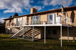 Rear view of house with stairs, brick siding, a lawn, and a chimney