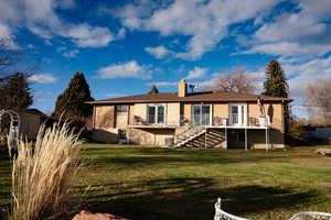 Back of property with stairs, brick siding, a lawn, a chimney, and a deck