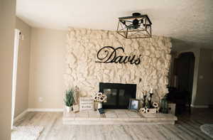 Unfurnished living room featuring a textured ceiling, a stone fireplace, arched walkways, and wood finished floors