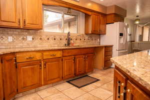 Kitchen with brown cabinetry, light stone counters, tasteful backsplash, light tile patterned floors, and a textured ceiling