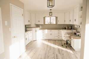 Kitchen featuring open shelves, built in study area, white cabinetry, and pendant lighting