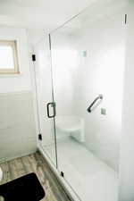 Full bathroom with light wood-type flooring, a shower stall, tile walls, and wainscoting