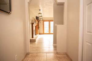 Hall with light tile patterned floors, a textured ceiling, french doors, and arched walkways
