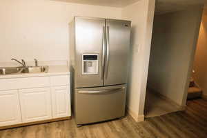 Kitchen with stainless steel fridge, white cabinets, light countertops, and light wood-style floors