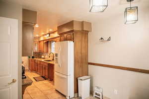Kitchen featuring tasteful backsplash, white refrigerator with ice dispenser, light tile patterned flooring, brown cabinets, and recessed lighting