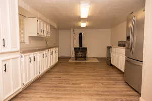 Kitchen with stainless steel appliances, white cabinets, a wood stove, a textured ceiling, and light countertops