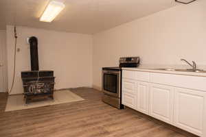 Kitchen with a wood stove, white cabinets, stainless steel range with electric stovetop, light countertops, and concrete block wall