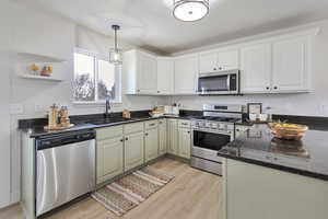 Kitchen featuring appliances with stainless steel finishes, dark stone countertops, white cabinetry, and hanging light fixtures
