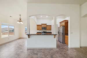 Kitchen with brown cabinets, appliances with stainless steel finishes, a chandelier, a kitchen bar, and decorative light fixtures