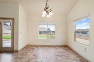 Unfurnished dining area featuring a chandelier, lofted ceiling, healthy amount of natural light, and light tile patterned floors