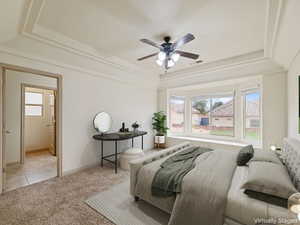 Bedroom with a tray ceiling, light colored carpet, a ceiling fan, and connected bathroom