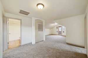 Additional living space with light carpet and vaulted ceiling