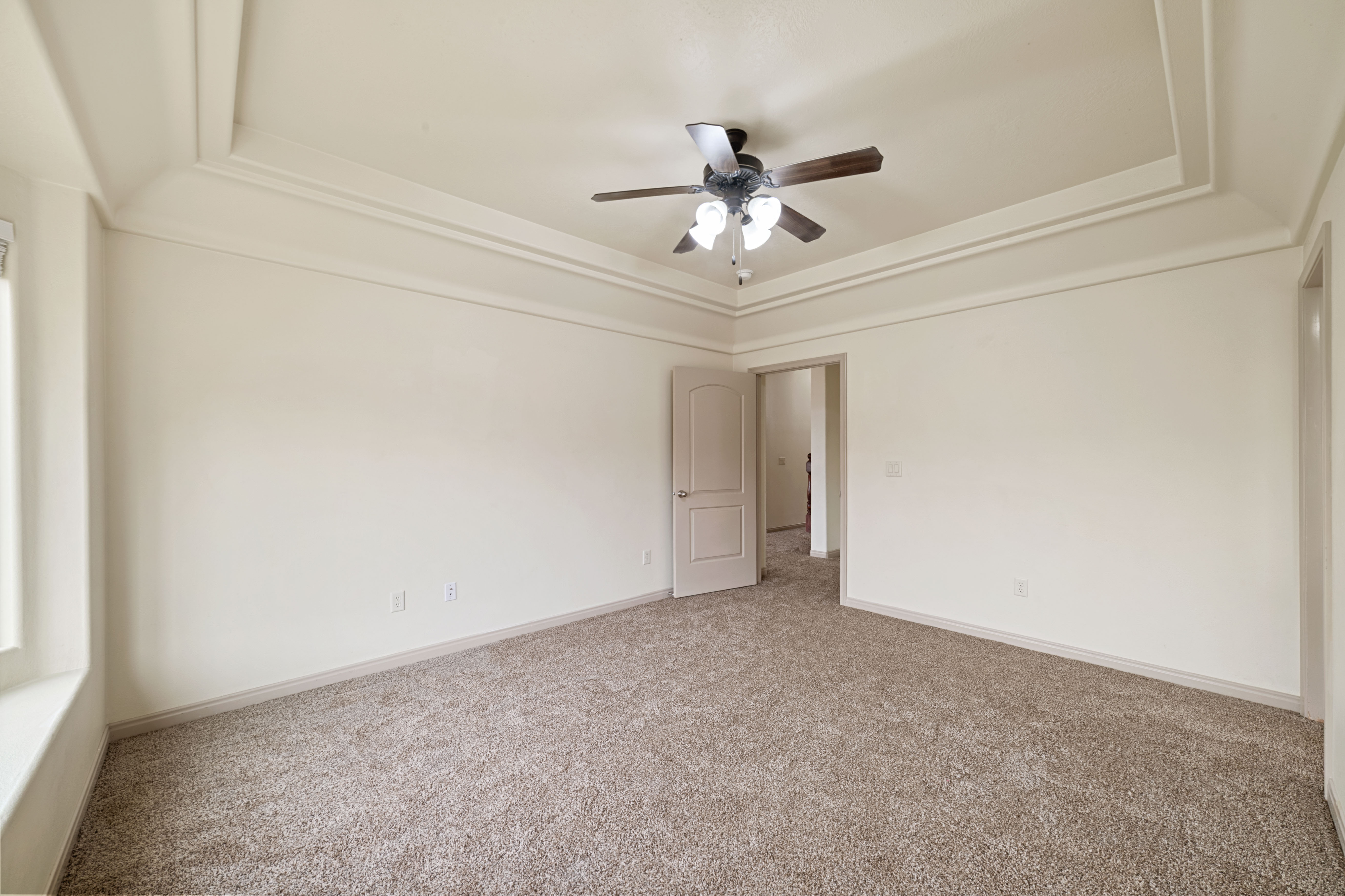 Carpeted empty room with a raised ceiling and ceiling fan