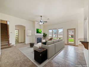 Living area with arched walkways, a tiled fireplace, stairs, and a ceiling fan