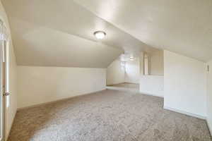 Bonus room with light carpet, a textured ceiling, and lofted ceiling