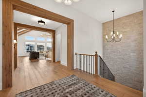 Hall with a chandelier, light wood-style floors, an upstairs landing, and vaulted ceiling