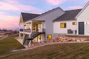 Rear view of property featuring a patio, a shingled roof, stairway, and a lawn