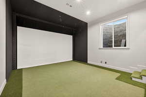 Carpeted home theater with golf simulator and an area to practice putting