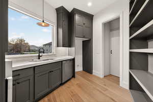 Kitchen with hanging light fixtures, dishwasher, light wood-type flooring, open shelves, and light stone counters